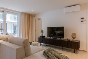 Ein modernes Wohnzimmer mit großem Flachbildfernseher, einer Couch, einem Couchtisch und einem Beistelltisch mit Pflanze.