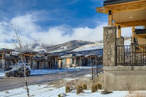 A modern building with a stone facade, a covered outdoor area, and a view of snow-covered mountains. - Luxurious 4-Bedroom RetreatClose to Deer Valley East Village 1936 4 Home (Heber City)