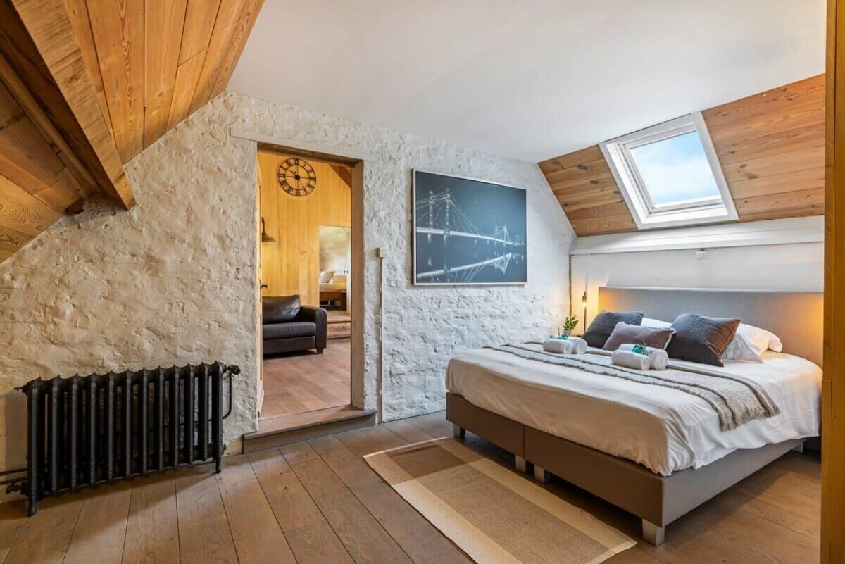 A bedroom with a sloped ceiling, a bed, a radiator, a clock, and a framed picture on the wall.