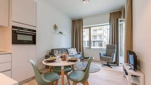 A modern living room with a dining area, a sofa, a TV, and a window with a view of buildings. - Coastal retreat w/ terrace & self check-in (Oostende)