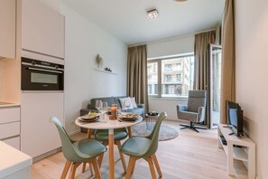 Una sala de estar moderna con comedor, un sofá, un televisor y un ventanal con vistas a edificios.