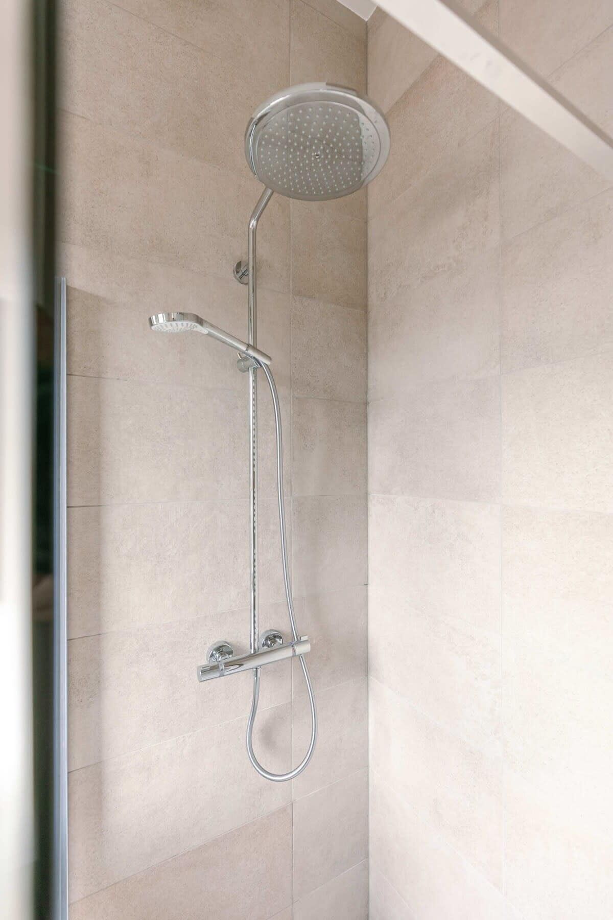 Ducha con cabezal de ducha de mano y panel de control en la pared.