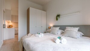 A bedroom with a bed, white curtains, a bedside table, a nightstand, and a wall-mounted shelf with a plant. - Coastal retreat w/ terrace & self check-in (Oostende)