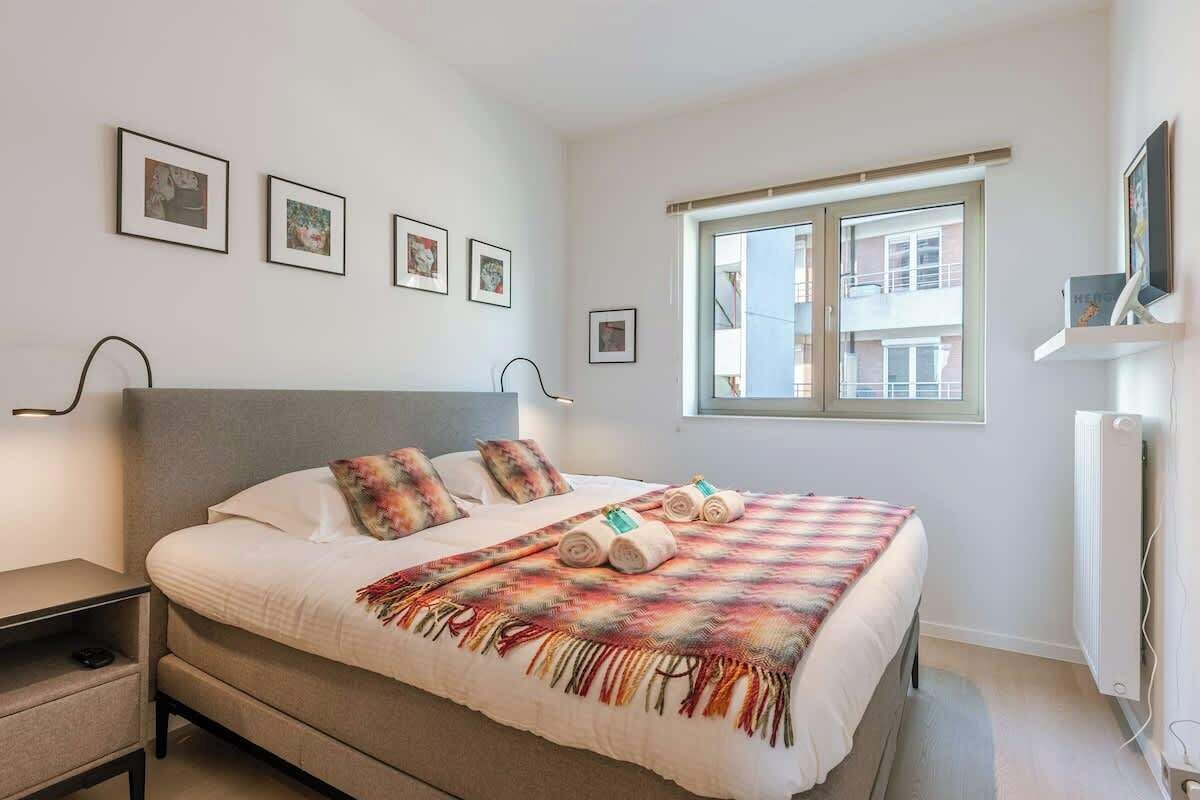 A bedroom with a bed, bedside tables, a window, and wall-mounted artwork.