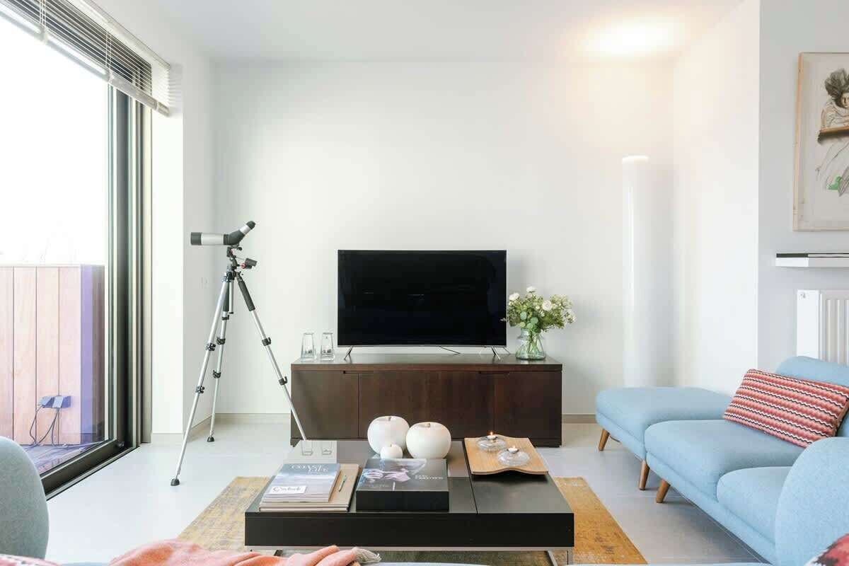A living room with a TV on a wooden cabinet, a tripod, and a blue sofa.
