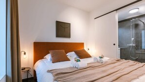 Una habitación de hotel con cama, mesita de noche, reloj de pared y zona de ducha.