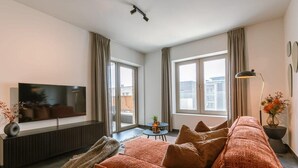 Una sala de estar moderna con sofá, televisión y ventanas grandes.