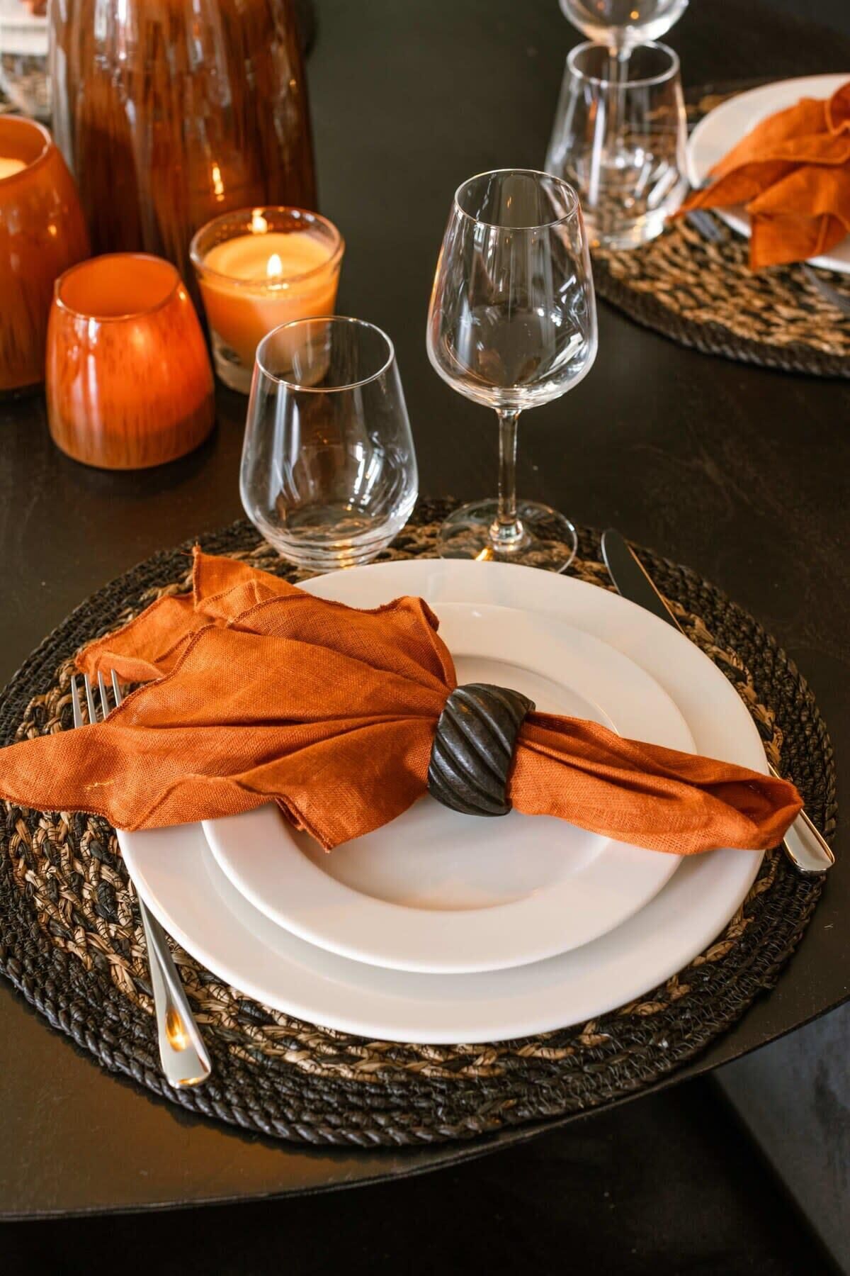 A table set with a white plate, a folded orange napkin, and a metal fork.