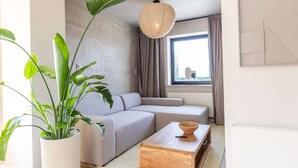 Una sala de estar moderna con un sofá, una mesa de centro de madera, una planta en maceta y un lámpara colgante.
