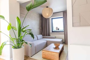 Ein modernes Wohnzimmer mit einer Couch, einem Holztisch, einer Zimmerpflanze und einer Hängelampe.