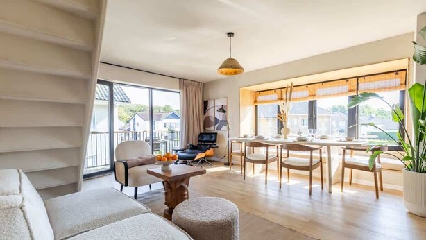 Una sala de estar moderna con sofá, reposapiés, mesa de comedor, sillas y televisor.