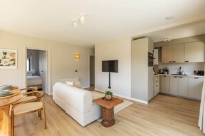 Una sala de estar moderna con un sofá blanco, una mesa de comedor de madera y una zona de cocina con armarios y electrodomésticos.