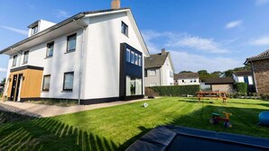 Une maison moderne à deux étages, dotée d’une pelouse bien entretenue et d’une structure de jeu en bois.