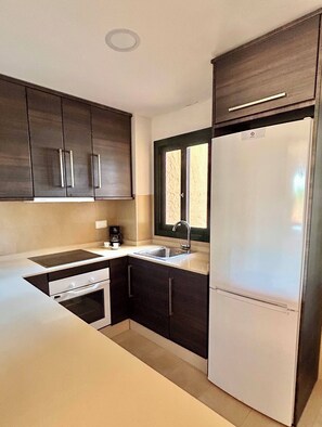 A modern kitchen with dark cabinets, a white countertop, a built-in oven, and a stainless steel refrigerator. - Luxury apartment on golf resort with private plunge pool (MC)