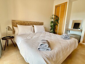 A neatly made bed with a headboard, a bedside table with a lamp, a folded towel on the bed, and a potted plant beside the bed. - Luxury apartment on golf resort with private plunge pool (MC)