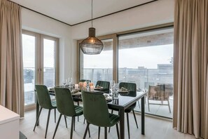 A dining area with a table set for six, large windows, and a hanging light fixture. - Coastal apartment w/ balcony & parking (Oostende)
