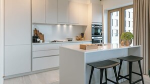 Una cocina moderna con armarios blancos, una isla central con taburetes y un ventanal con cortinas.