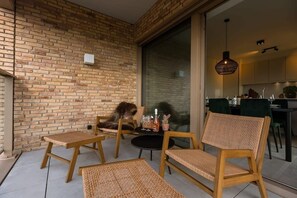 Un espace extérieur moderne, aménagé avec des meubles en osier, un mur en briques et une porte-fenêtre coulissante donnant sur une cuisine.