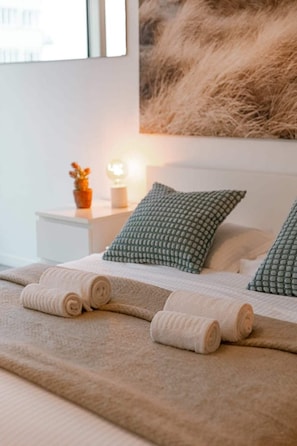 Un lit bien fait, avec des serviettes pliées, une table de chevet avec une lampe et un tableau accroché au mur.