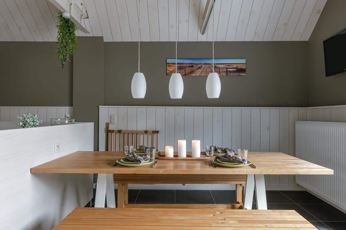 A dining area with a wooden table, white chairs, hanging pendant lights, and a bench.