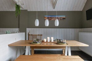 Een eetgedeelte met een houten tafel, witte stoelen, hangende hanglampen en een bank.