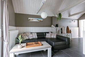 Een moderne woonkamer met een zwarte leren bank, een witte salontafel en een hangplant.