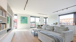 A modern living room with a sofa, bookshelf, and large windows. - Bright 2BR apartment w/ balcony & private entrance (Gent)