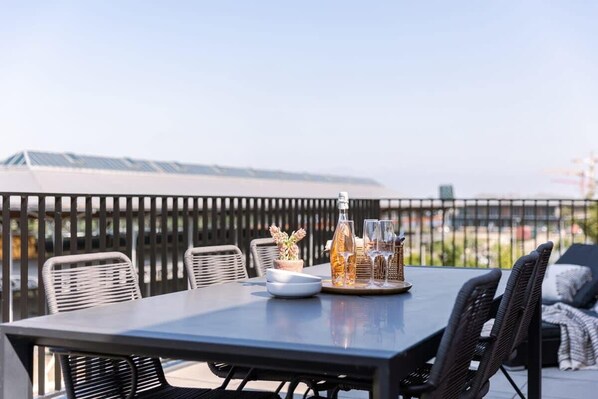 A rooftop terrace with a table set for dining, surrounded by wicker chairs, and a view of the cityscape.