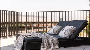 A balcony with a black lounge chair, a small ottoman, and a knitted throw blanket. - Bright 2BR apartment w/ balcony & private entrance (Gent)