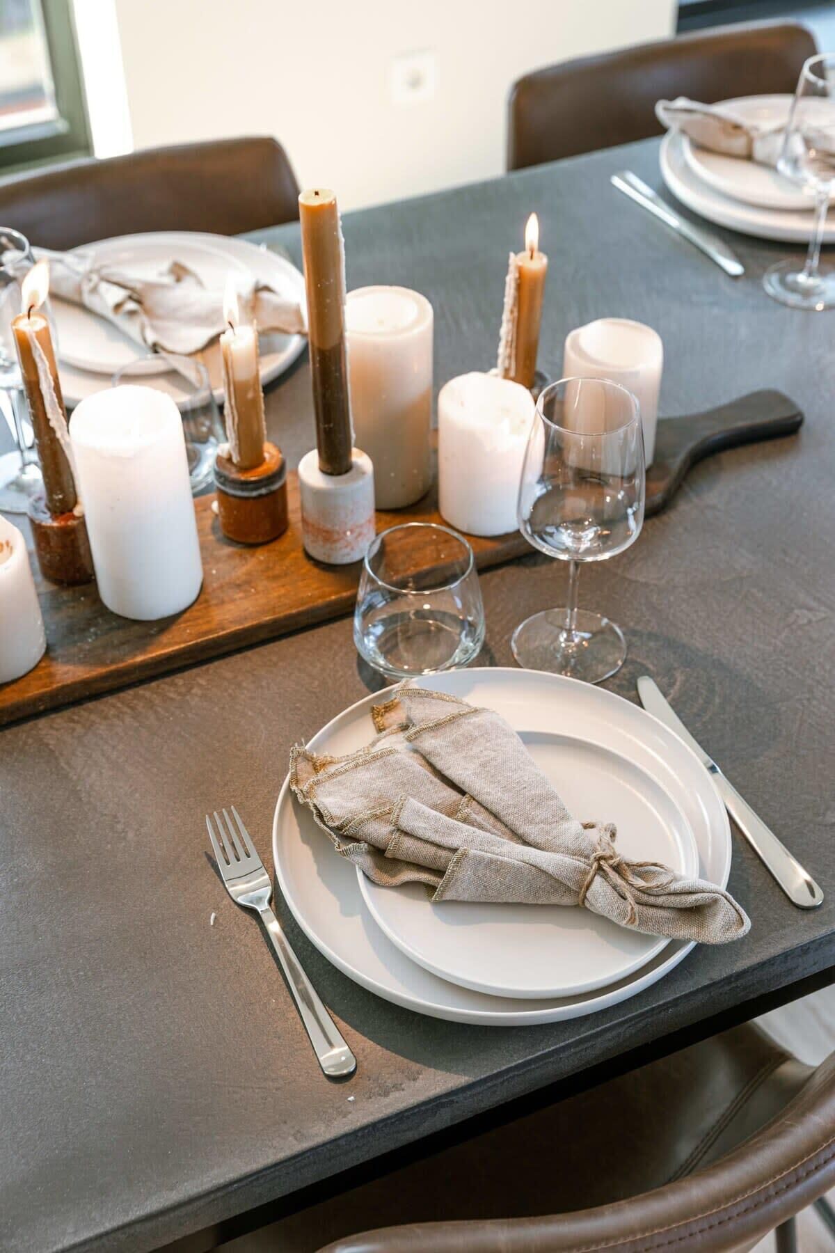 A dining table set with plates, cutlery, candles, and glasses.