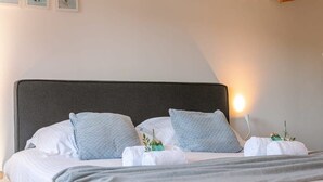 Un lit bien fait, avec du linge de lit blanc et deux coussins à motifs, une table de chevet avec une lampe et un tableau accroché au mur.