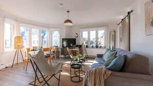 Un salon moderne comprenant un canapé, des fauteuils, un téléviseur et un coin repas avec une table et des chaises.