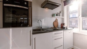 Une cuisine moderne avec des meubles blancs, un four en acier inoxydable, un lave-vaisselle et une fenêtre donnant sur des immeubles.