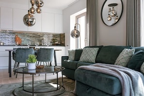 A modern living room with a green sofa, a round coffee table, and a dining area with chairs and a glass-top table. - 1BR unit w/ parking & elevator (Oostende)