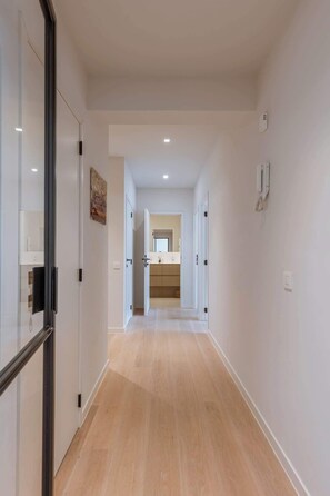 Ein Flur mit Holzboden, weißen Wänden und einem im Hintergrund sichtbaren Badezimmer.