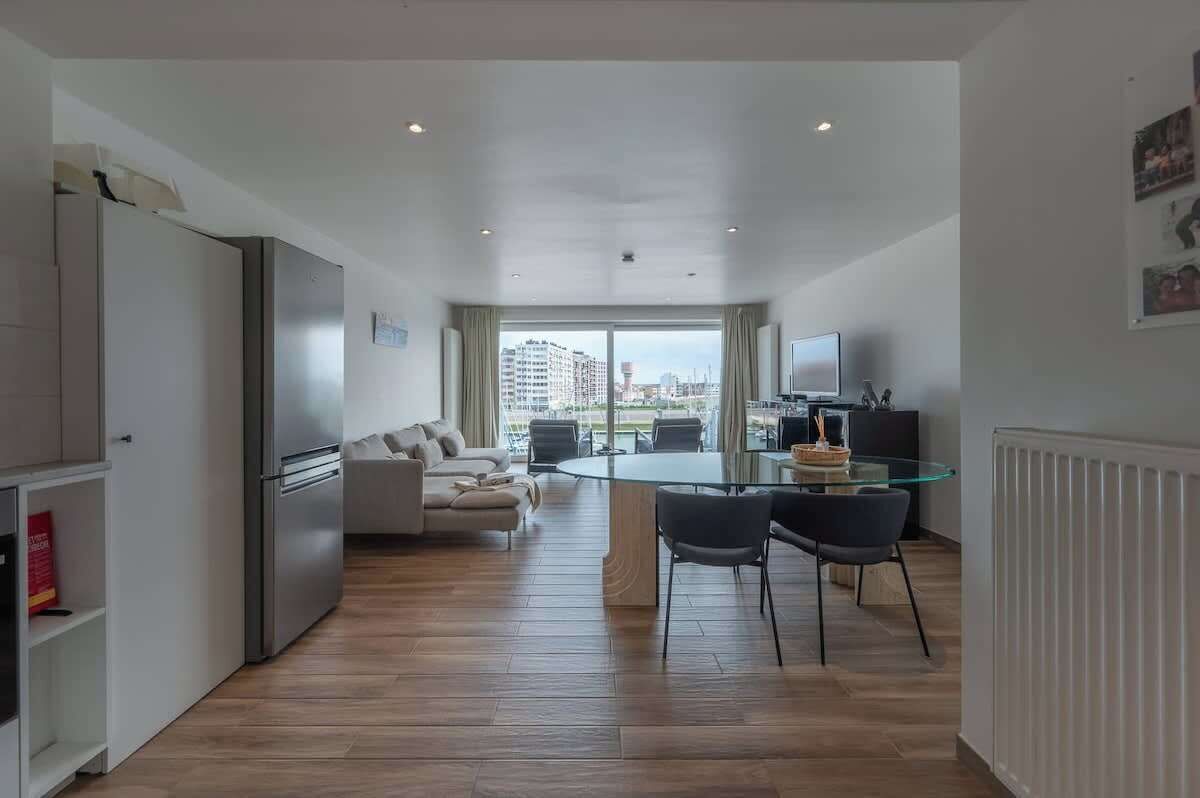 A modern apartment with a dining area, kitchen, and a large window offering a city view.