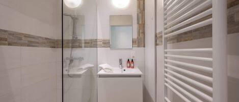 Ein modernes Badezimmer mit Duschkabine aus Glas, einem weißen Waschbecken mit Spiegel und einem Handtuchhalter.