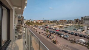 A balcony with a view of a marina, parked cars, and buildings in the background. - Waterfront studio w/ private entrance (Blankenberge)