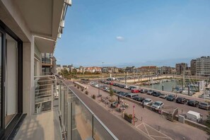Ein Balkon mit Blick auf einen Yachthafen, geparkte Autos und Gebäude im Hintergrund.