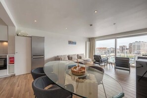 Ein moderner Wohnraum mit einem Glastisch, einer Sofagarnitur und Blick auf die Stadt durch große Fenster.