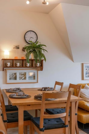 Ein Essbereich mit Holztisch, Stühlen, einer Uhr, einem Blumentopf und einem Regal mit Tassen.