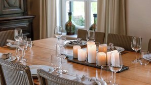 A dining table set with candles, glasses, and plates, with a view of bottles and curtains in the background.