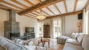 A living room with a fireplace, sofa, television, and wooden beams.