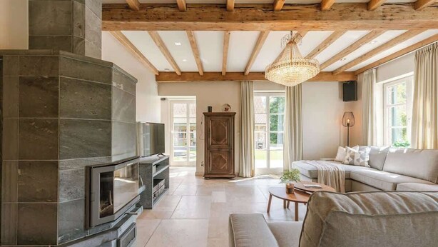 A living room with a stone fireplace, wooden beams, a chandelier, a sofa, and a television.
