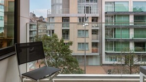 A balcony with a chair, a table, and a view of a multi-story building with balconies. - Casiola coastal stay - parking & terrace (Knokke-Heist)