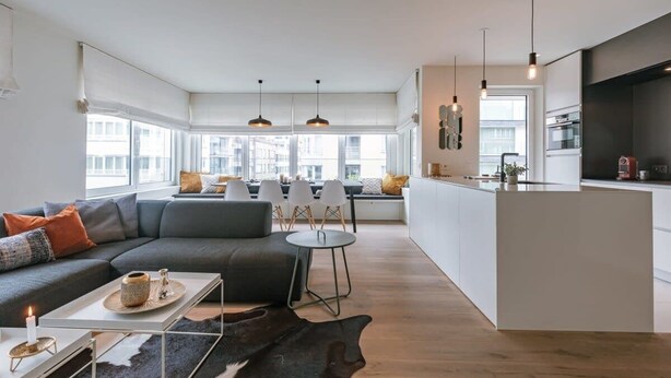 A modern living room with a sofa, a coffee table, and a dining area with chairs. - Casiola coastal stay - parking & terrace (Knokke-Heist)