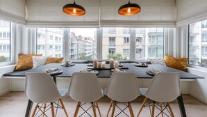 A dining area with a long table, four chairs, and pendant lights. - Casiola coastal stay - parking & terrace (Knokke-Heist)