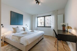 Ein modernes Schlafzimmer mit Bett, Nachttisch, Schreibtisch, Stuhl und einem großen Fenster.