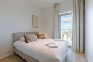 A modern bedroom with a large bed, a view of the city, and a minimalist decor. - 9th-floor apartment w/ terrace & scenic views (Oostende)