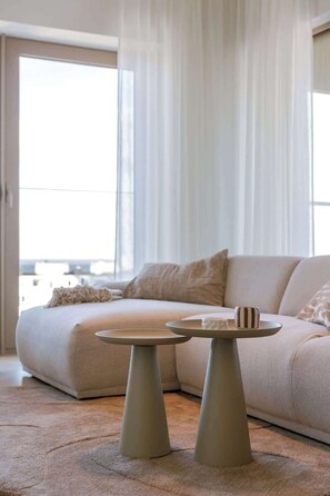 A modern living room with a sofa, two tables, and a view through large windows. - 9th-floor apartment w/ terrace & scenic views (Oostende)